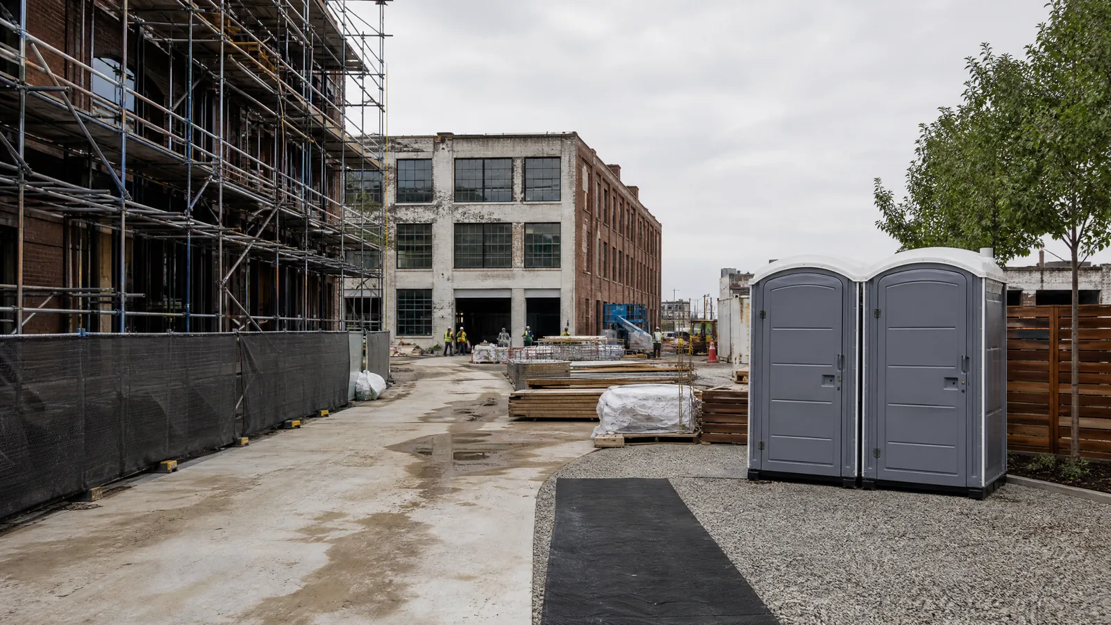 Portable toilet positioned on a firm surface beside a fenced urban construction site